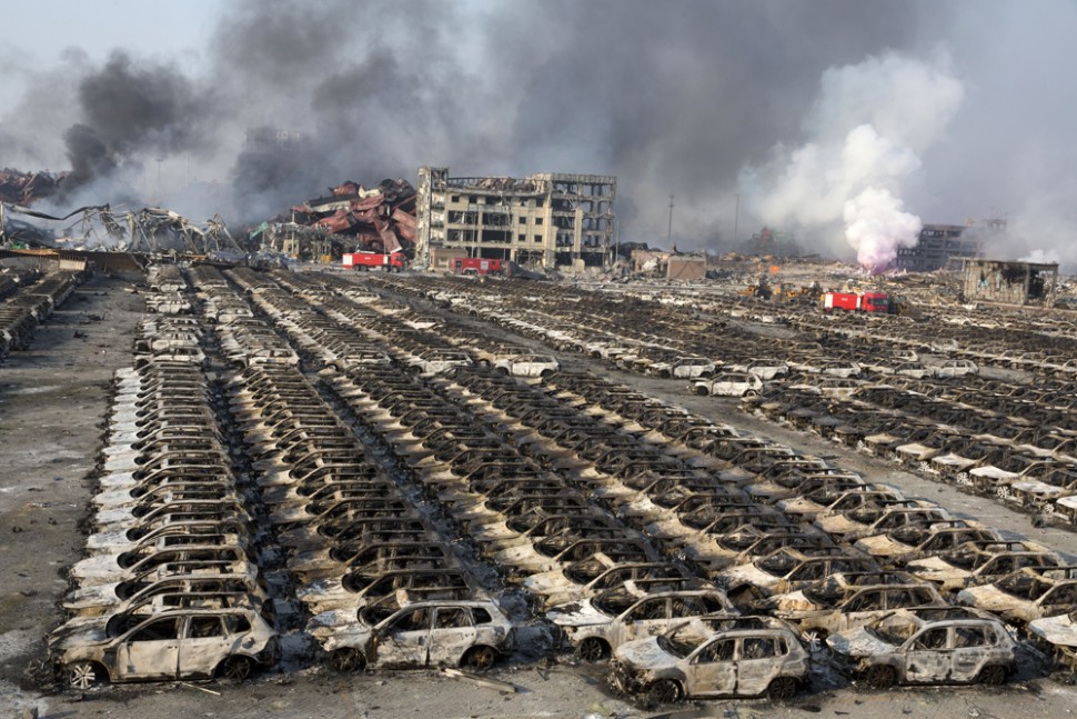 Smoke billows from the site of an explosion that reduced a parking lot filled with new cars to charred remains at a warehouse in northeastern China's Tianjin municipality, Thursday, Aug. 13, 2015. Huge explosions in the warehouse district sent up massive fireballs that turned the night sky into day in the Chinese port city of Tianjin, officials and witnesses said Thursday. (AP Photo/Ng Han Guan)
