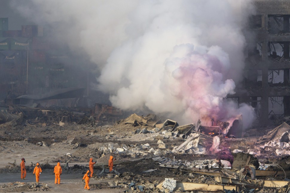 Fire fighters in protective gear watch partially pink smoke continue to billow after an explosion at a warehouse in northeastern China's Tianjin municipality, Thursday, Aug. 13, 2015. Huge, fiery blasts at a warehouse for hazardous chemicals killed many people and turned nearby buildings into skeletal shells in the Chinese port of Tianjin, raising questions Thursday about whether the materials had been properly stored. (AP Photo/Ng Han Guan)