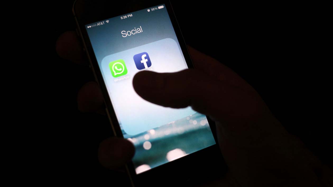 Celular no escuro com ícones de aplicativos WhatsApp e Facebook