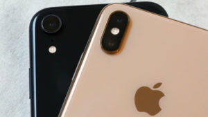 Dois iPhones, um preto e um dourado, empilhados, com a parte de trás virada para cima. O logo da Apple do iPhone dourado está à mostra.