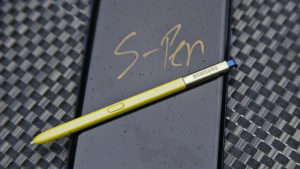 Foto de aparelho Galaxy Note 9, da Samsung, com sua caneta stylus apoiada sobre a tela. Na tela, está escrito S-Pen em amarelo sobre fundo preto.