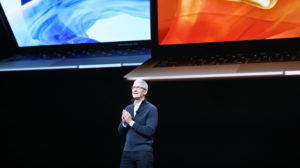 Tim Cook, CEO da Apple, em uma apresentação da empresa. Ao fundo, um telão mostra dois notebooks da marca.