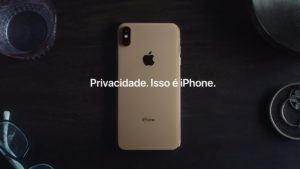 captura de tela de propaganda de tv do iphone. sobre uma mesa de madeira, está um iphone dourado. ele está virado de frente para a mesa, com as costas viradas para cima. em cima dele, está um grafismo com a frase "Privacidade. Isso é iPhone."