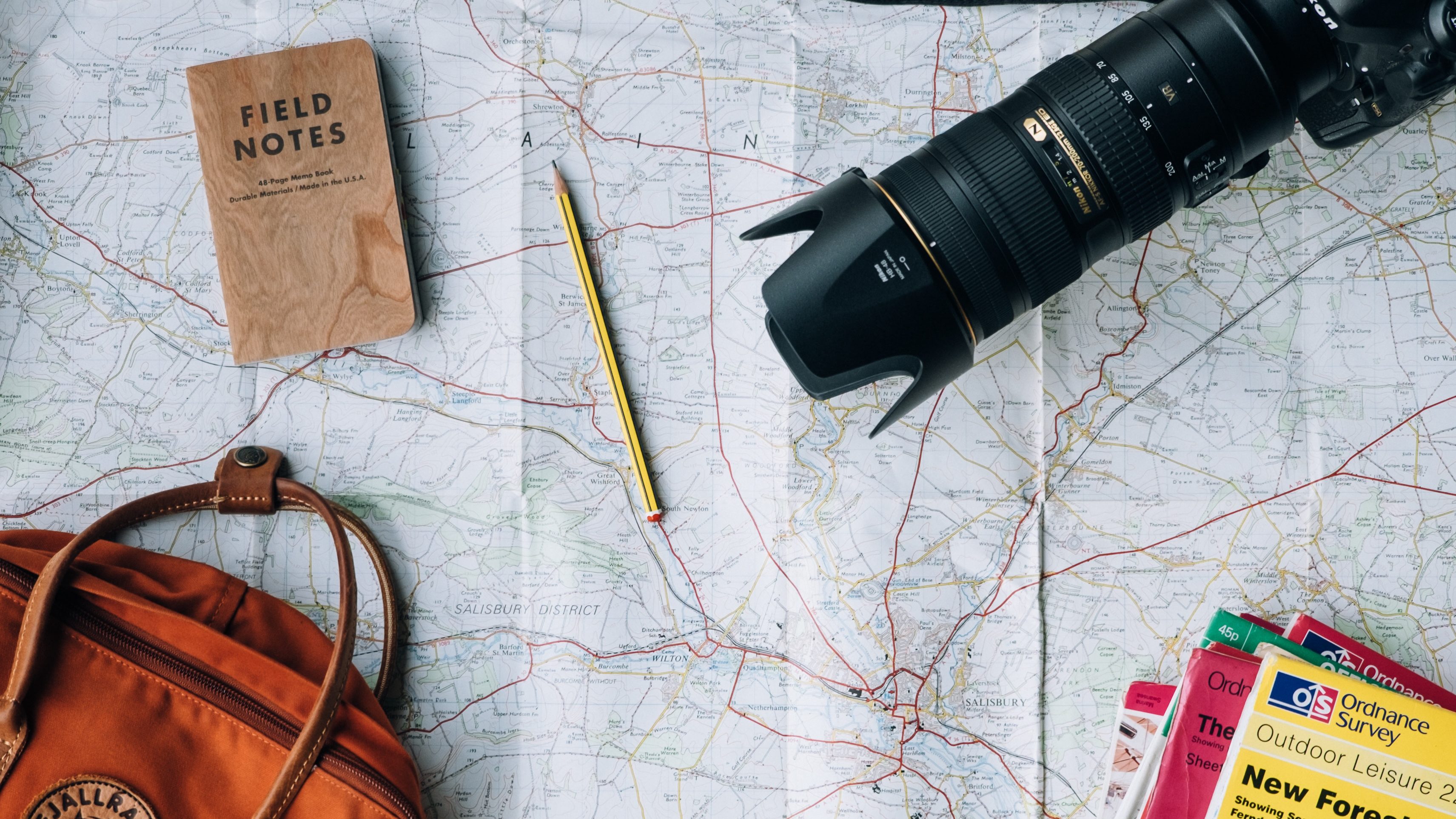 Mapa com um lápis, um caderno, uma câmera, uma bolsa e guias de viagem sobre ele.