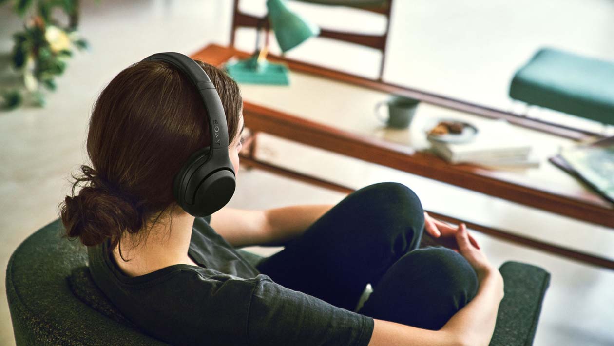 Mulher sentada usando os fones de ouvido Sony XB900N