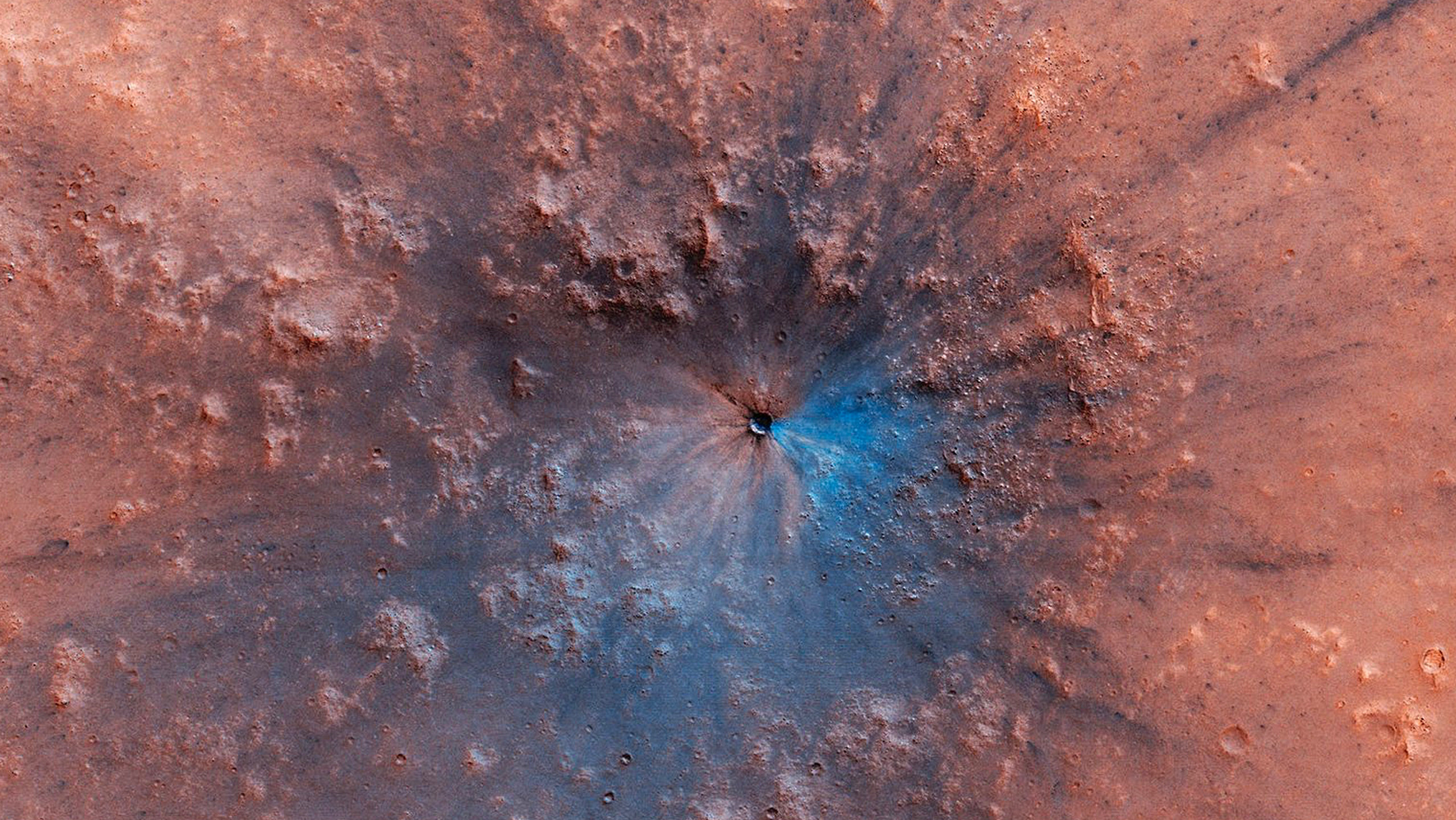 Imagem em falsa cor da nova cratera descoberta em marte. A superfície do planeta é vermelha, há um círculo de relevo acidentado e um buraco no meio, com metade desse buraco pintado de azul. Não é a cor real, é só um indicativo de