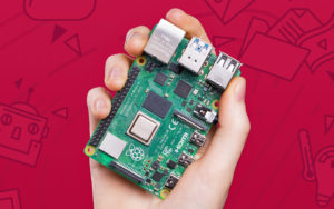 Um Raspberry Pi 4 na mão de uma criança. Ele é uma placa verde, com vários componentes metálicos prateados em suas bordas para conectar outros componentes.