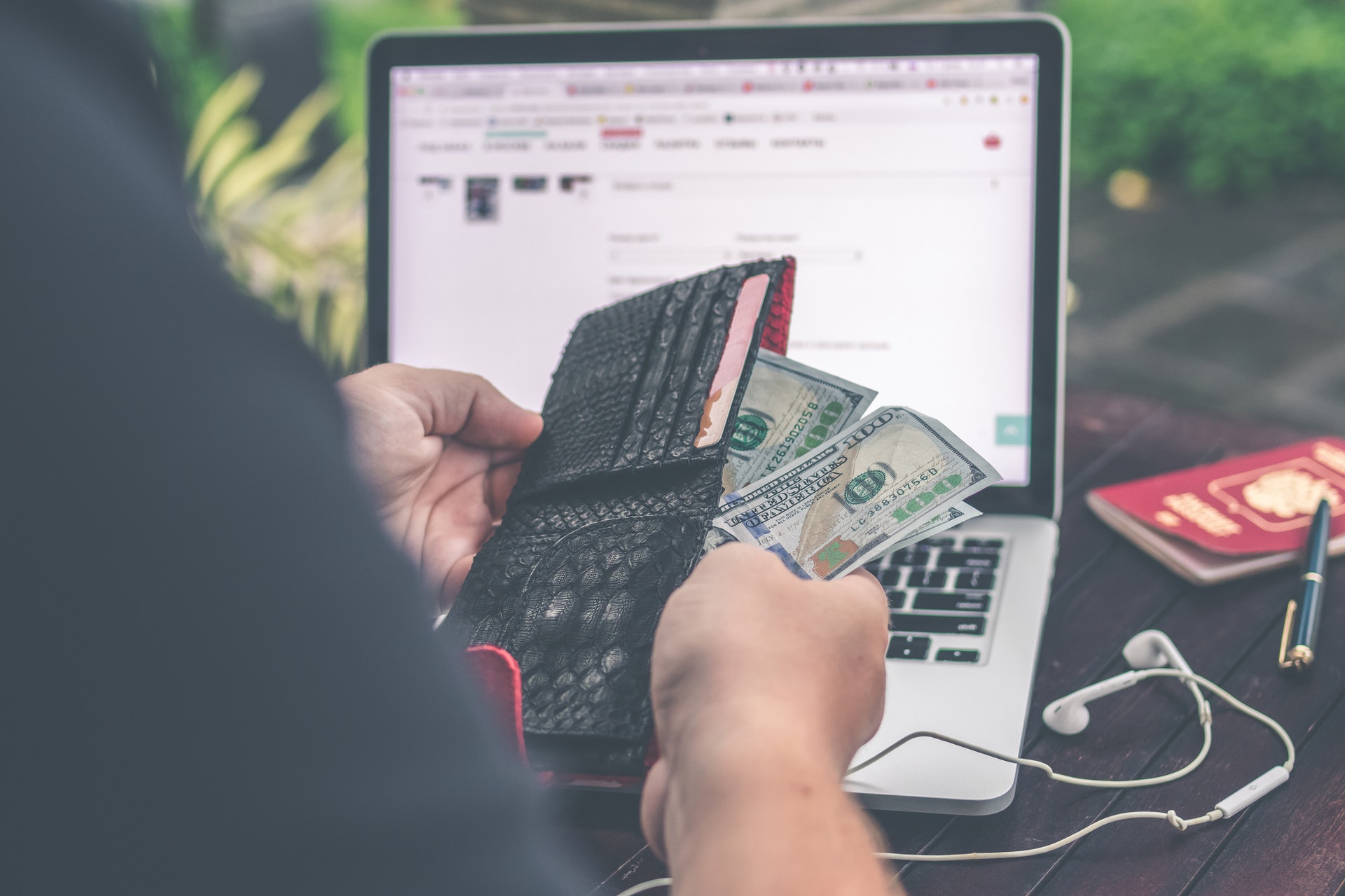 Pessoa segurando carteira com dinheiro em frente a um laptop