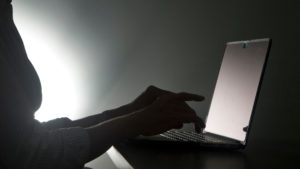 Pessoa digita em um laptop em um ambiente mal iluminado