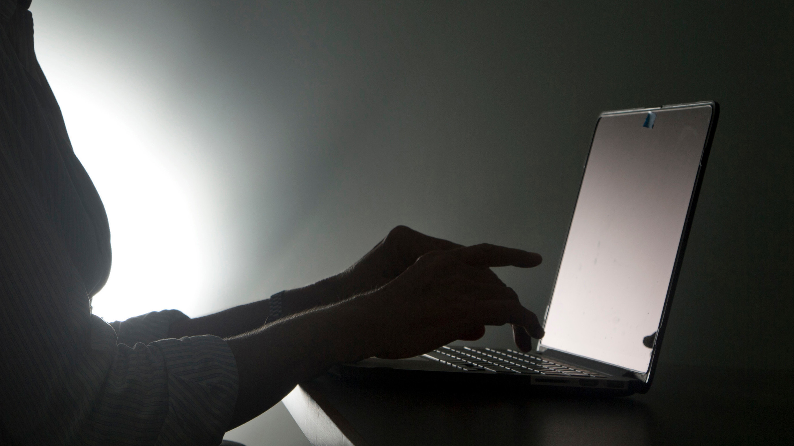 Pessoa digita em um laptop em um ambiente mal iluminado