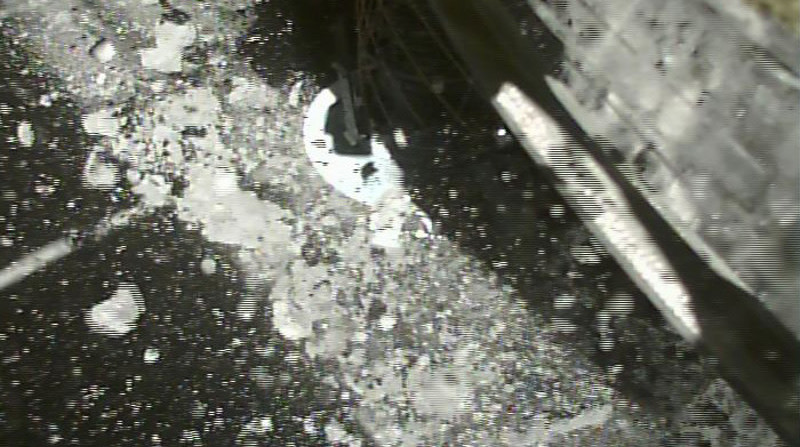 Imagem preto e branco mostra uma estrutura mecânica pousando em um chão rochoso, com pequenas pedras suspensas.