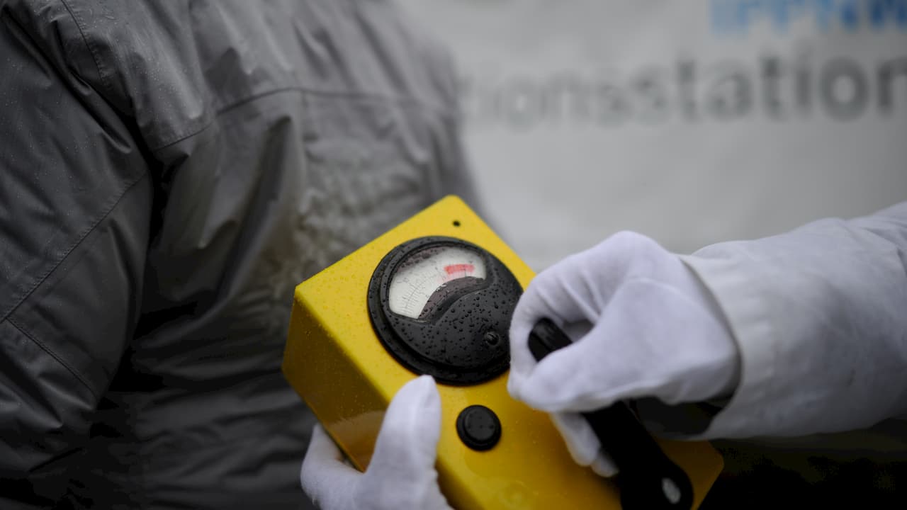 Medidor de radiação. Foto mostra um aparelho retangular amarelo com um mostrador redondo com ponteiro seundo segurado por uma mão com uma luva branca.