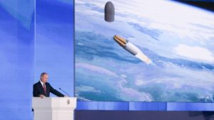 Presidente da Rússia, Vladimir Putin, em uma tribuna. Ao fundo, uma tela mostra a imagem de um míssil voando em uma grande altitude.