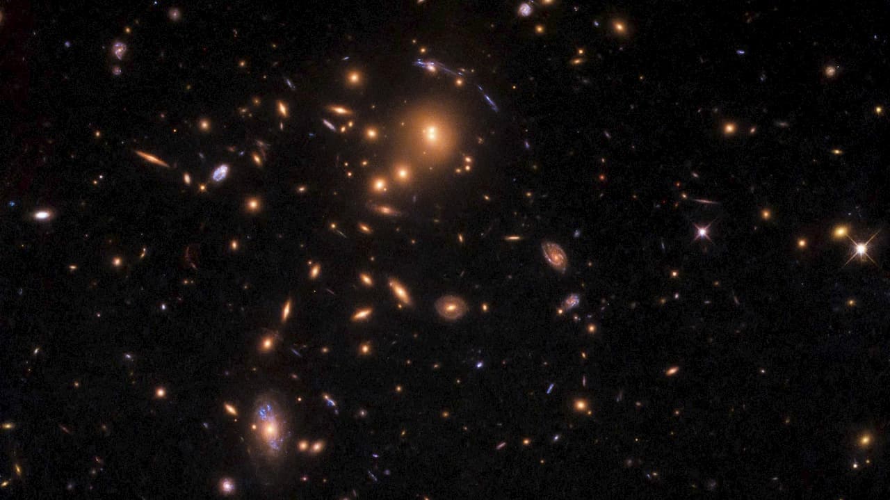 Imagem de aglomerado de galáxias mostra pontos luminosos alongados.