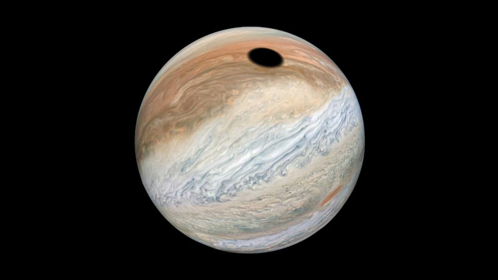 Júpiter (uma esfera com nuvens acinzentadas e avermelhadas) com um círculo preto na parte superior.