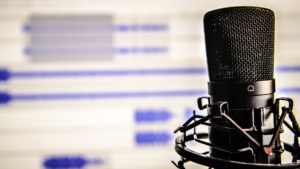 Microfone com trilhas de áudio exibidas em tela de computador em segundo plano