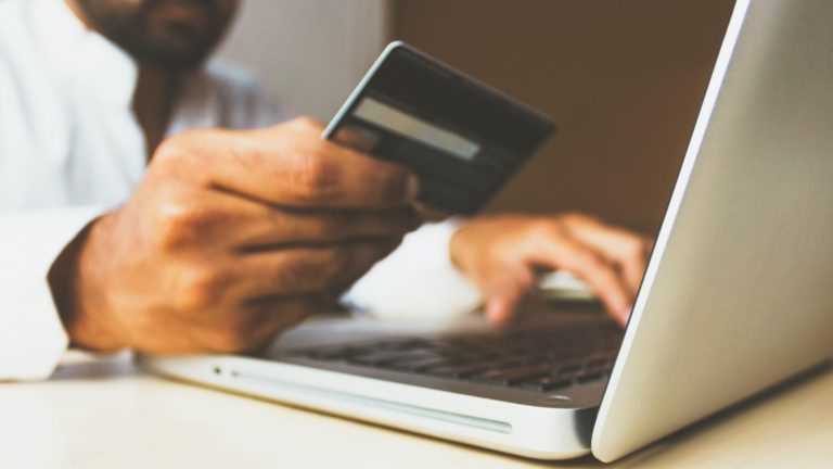 Pessoa segurando cartão de crédito em frente a um laptop