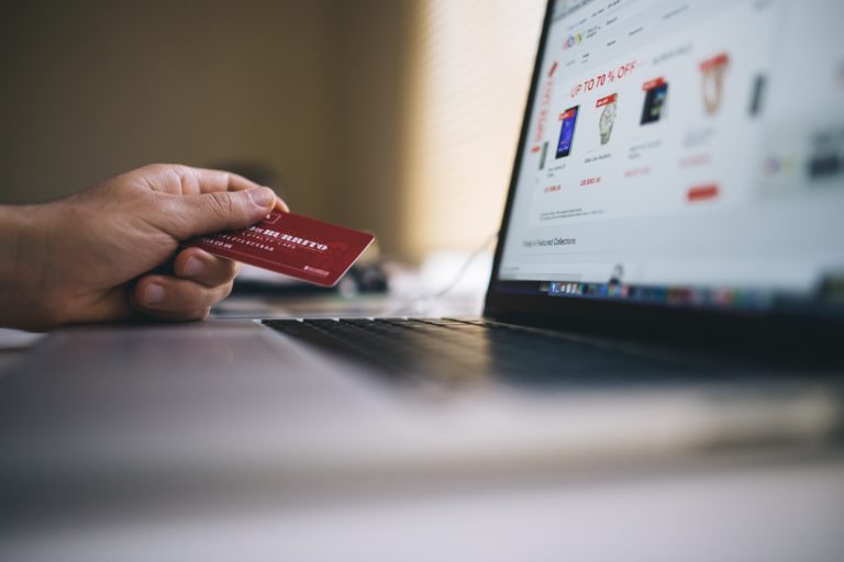 Mão segurando cartao de crédito em frente a laptop