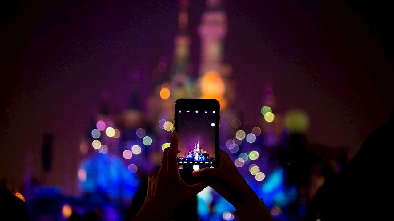 turista tira uma foto com um iPhone na Disneylândia de Xangai.