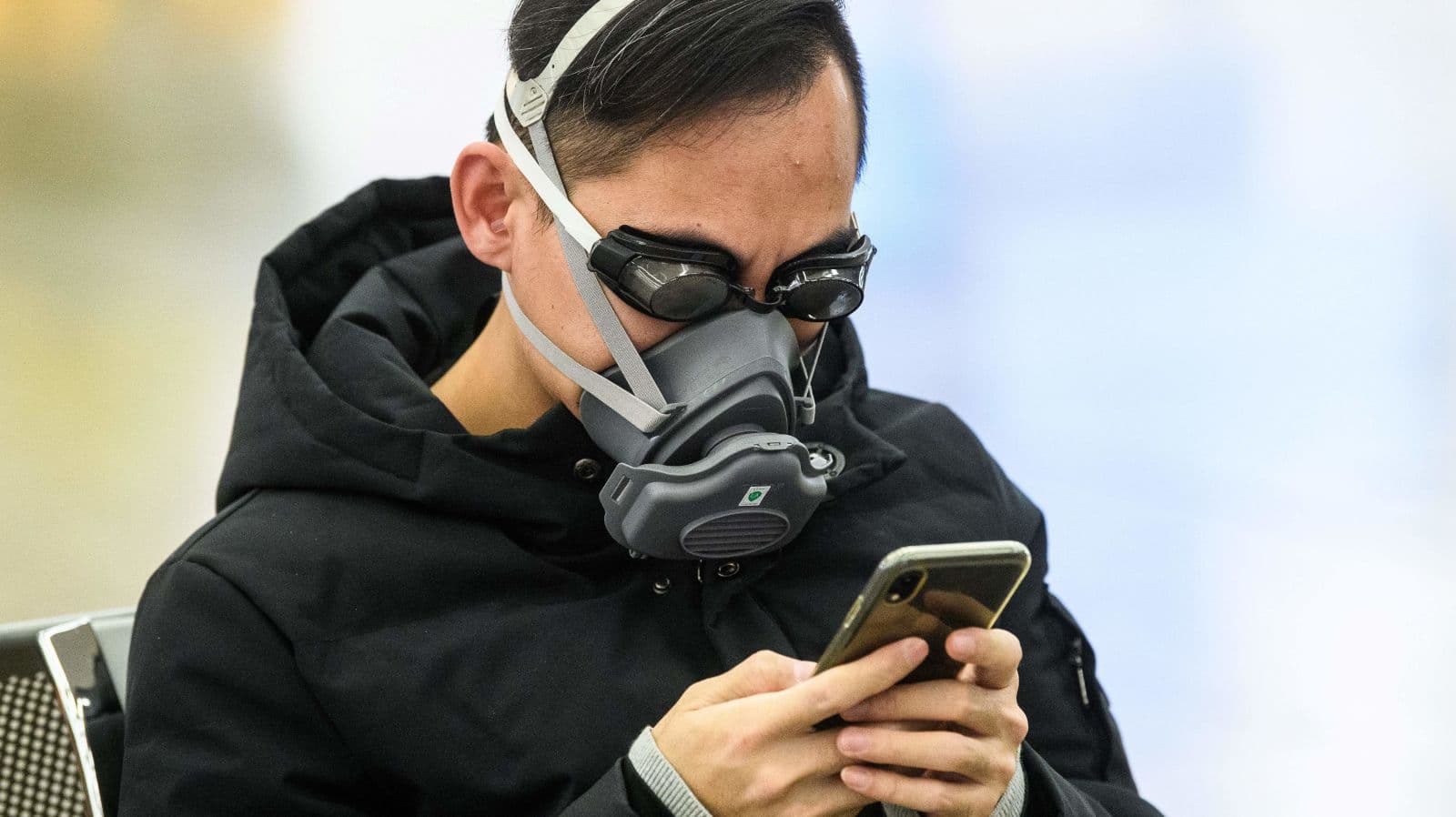 Homem se protege do coronavírus com máscara no rosto e óculos de natação enquanto usa o celular
