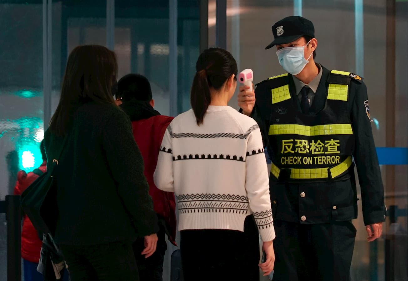 Funcionário de um aeroporto usa uma pistola de temperatura para verificar as pessoas que saem do Aeroporto Internacional de Wuhan Tianhe estão com febre