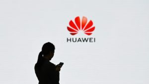 Pessoa mexendo em celular com o logo da Huawei ao fundo