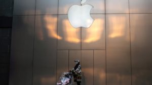 Pessoa com máscara e um carrinho de bebê sob fachada da Apple