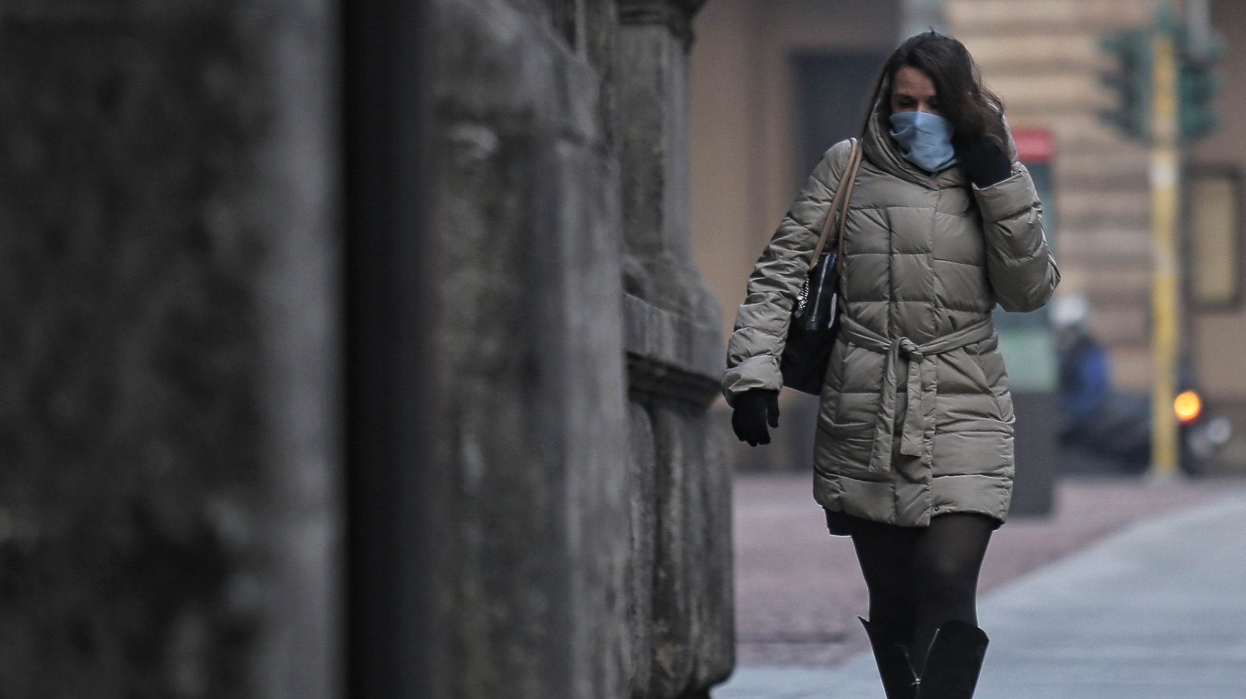 Mulher caminha em rua usando máscara de proteção facial. Crédito: Getty Images