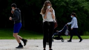 Mulher usa smartphone em espaço público enquanto está de máscara