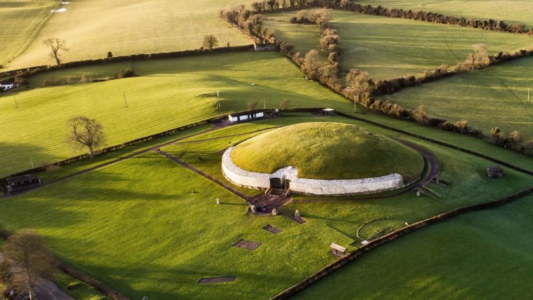 Foto de campo aberto com uma construção circular de bordas brancas e cobertura vegetal.