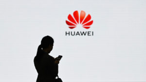 Mulher segurando smartphone é fotografada com o logotipo da Huawei. Crédito: Wang Zhao/Getty Images