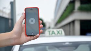 Pessoa segura celular com app da Uber em frente a um táxi