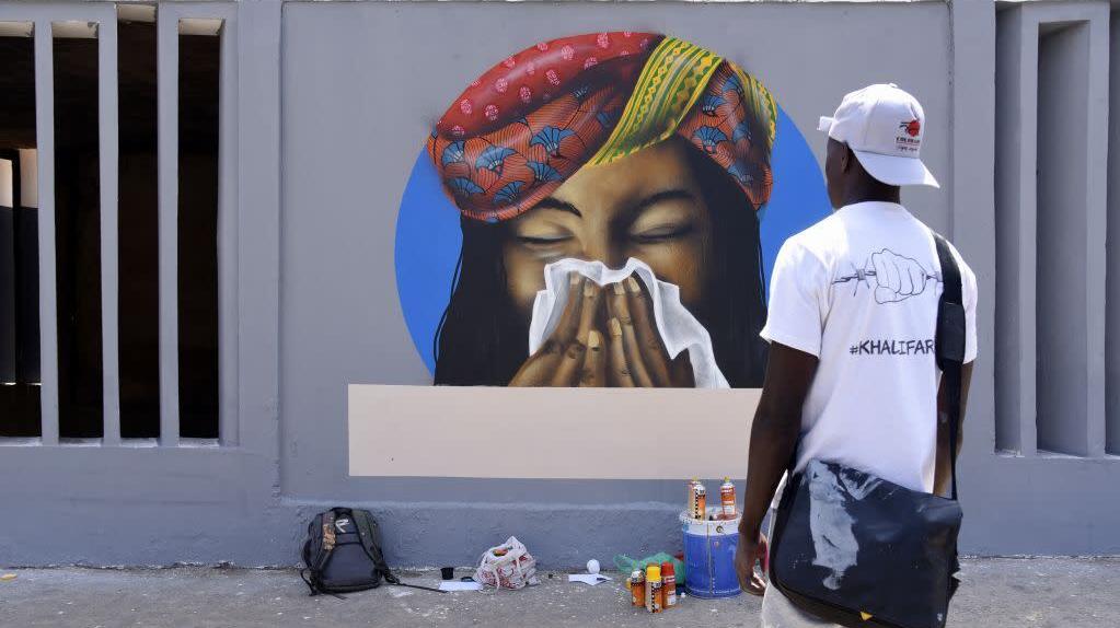 Homem observa grafite em muro em que mulher está espirrando. Crédito: Seyllou /AFP (Getty Images)