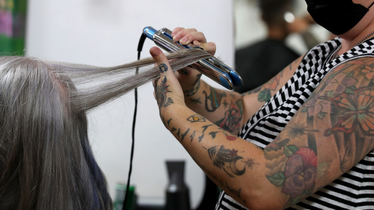 Cabeleireira alisa o cabelo de mulher em salão. Crédito: Justin Sullivan/Getty Images