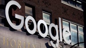 Logo do Google em metal na fachada de um prédio de tijolos marrom.