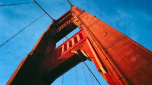 Detalhe da ponte Golden Gate, em San Francisco, Califórnia. Uma torre metálica vermelha se erguendo. Ao fundo, o céu azul.