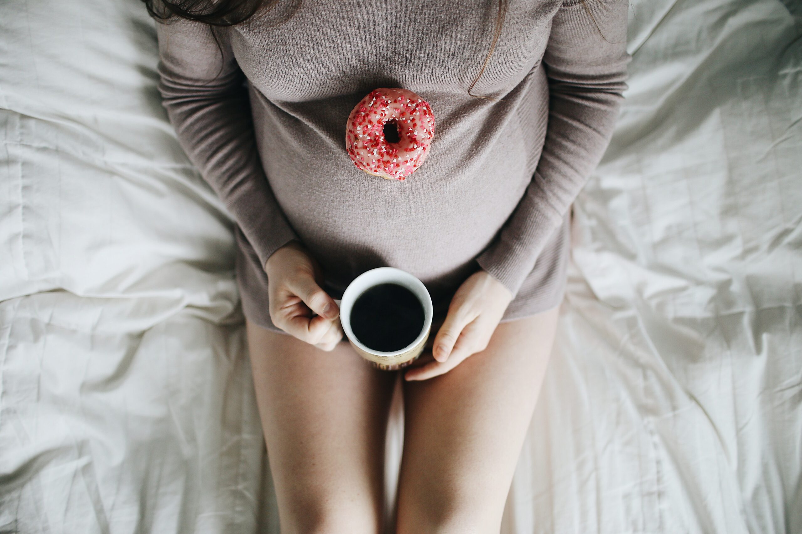 A imagem mostra uma mulher em estado avançado da gravidez apoiando uma xícara cheia de café em suas pernas
