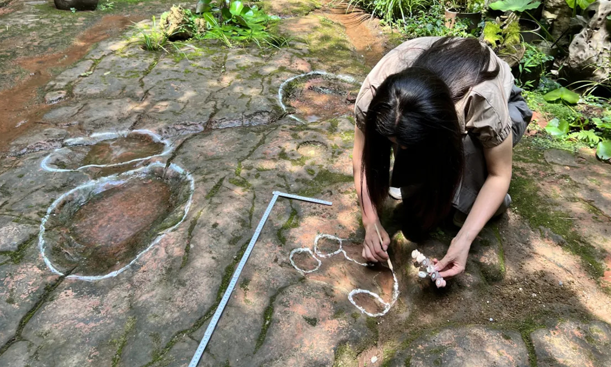 A imagem mostra a pesquisadora agachada no chão marcando as pegadas de dois dinossauros encontradas no restaurante chinês.