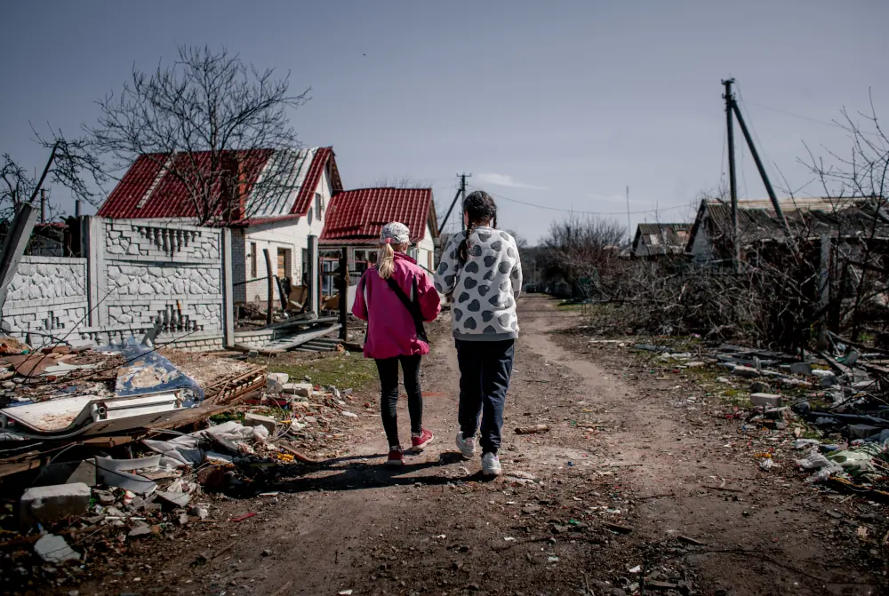Meninas caminham em meio aos destroços na cidade de Novoselivka, na Ucrânia.