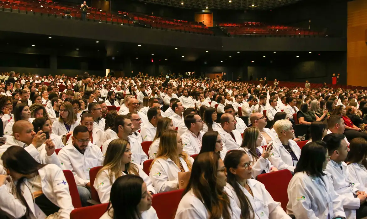 “A preocupação do conselho hoje é que se forme médicos de boa qualidade e com princípios éticos, a fim de atender à população”, completou. Desigualdade Apesar do significativo aumento no contingente de médicos brasileiros, o CFM considera que ainda há um cenário de desigualdade na distribuição, na fixação e no acesso aos profissionais. “O Brasil hoje tem número razoável de médicos registrados nos conselhos regionais de medicina, quando comparado às principais nações do mundo. Mas um dos principais problemas ainda é a distribuição desses médicos no país continental que é o Brasil”, avaliou Giamberardino. Os números mostram que a maioria dos profissionais opta por se instalar nos estados do Sul e do Sudeste e nas capitais, devido às condições de trabalho. Os que vivem no Norte, no Nordeste e em municípios mais pobres relatam falta de investimentos em saúde, vínculos precários de emprego e ausência de perspectivas. “Esse fato, por si só, trás muita dificuldade de acesso. Acesso é um princípio fundamental do Sistema Único de Saúde (SUS), adotado pelo Brasil em sua Constituição como direito do paciente”, destacou o conselheiro. “Se nós permitirmos que a medicina obedeça a uma lógica de mercado, atendendo às riquezas regionais, vamos promover desigualdade.” Perfil A idade média dos médicos em atividade no Brasil é 44,6 anos. Entre os homens, a idade média é 47,4 ano. Já para as mulheres, 42 anos. Observa-se também uma diferença no tempo de formação entre os gêneros: em média, os médicos têm 21 anos de formados, enquanto as médicas têm 16 anos. Em 2023, os homens ainda representavam, ligeiramente, a maioria entre os médicos com até 80 anos, respondendo por 50,08% do total, enquanto as mulheres representavam 49,92%. Em 2024, a estimativa é que o número de médicas ultrapasse o de médicos. Atualmente, entre os médicos com 39 anos ou menos, as mulheres já constituem maioria, representando 58% em comparação a 42% dos homens. “Se observarmos os profissionais hoje abaixo de 40 anos, a maioria é formada por mulheres”, destacou Giamberardino. “É uma característica das profissões. A mulher está impondo o seu justo papel de liderança e reconhecimento. Medicina se mede por conhecimento e só tem liderança na medicina quem tem conhecimento.” Distribuição O estudo mostra ainda que o aumento no número de médicos ao longo das últimas décadas não resultou em distribuição igualitária pelo país. O Sudeste tem proporção de profissionais superior à média nacional, de 2,81 por mil habitantes. A região tem a maior densidade e proporção de médicos; 3,76 por mil habitantes e 51% do total de médicos, enquanto abriga 41% da população brasileira. Em contraste, o Norte exibe a menor proporção de médicos (1,73 por mil habitantes), ficando significativamente abaixo da média nacional. O Nordeste, com 19,3% dos médicos e 26,8% da população, apresenta uma razão de 2,22 médicos por mil habitantes, também abaixo da média nacional. O Sul, por sua vez, com 15,8% dos médicos e 14,8% da população, registra 3,27 médicos por mil habitantes, enquanto o Centro-Oeste, com 9% dos médicos e 8,1% da população, tem 3,39 médicos por mil habitantes, ambos acima da média nacional. Nas capitais, a média de médicos por mil habitantes alcança o patamar de 7,03, contra 1,89 observada no conjunto das cidades do interior. Ao analisar os extremos dessa distribuição, Vitória registra a maior densidade: 18,68 médicos por mil habitantes. Em contrapartida, no interior do Amazonas, a densidade é de 0,20 médico por mil habitantes. “O número de médicos é razoável, mas ainda é mal distribuído. Se nós crescermos sem uma política de fixação, isso vai aumentar a desigualdade”, ressaltou Giamberardino. Brasil tem 575.930 médicos ativos: 2,81 por mil habitantes